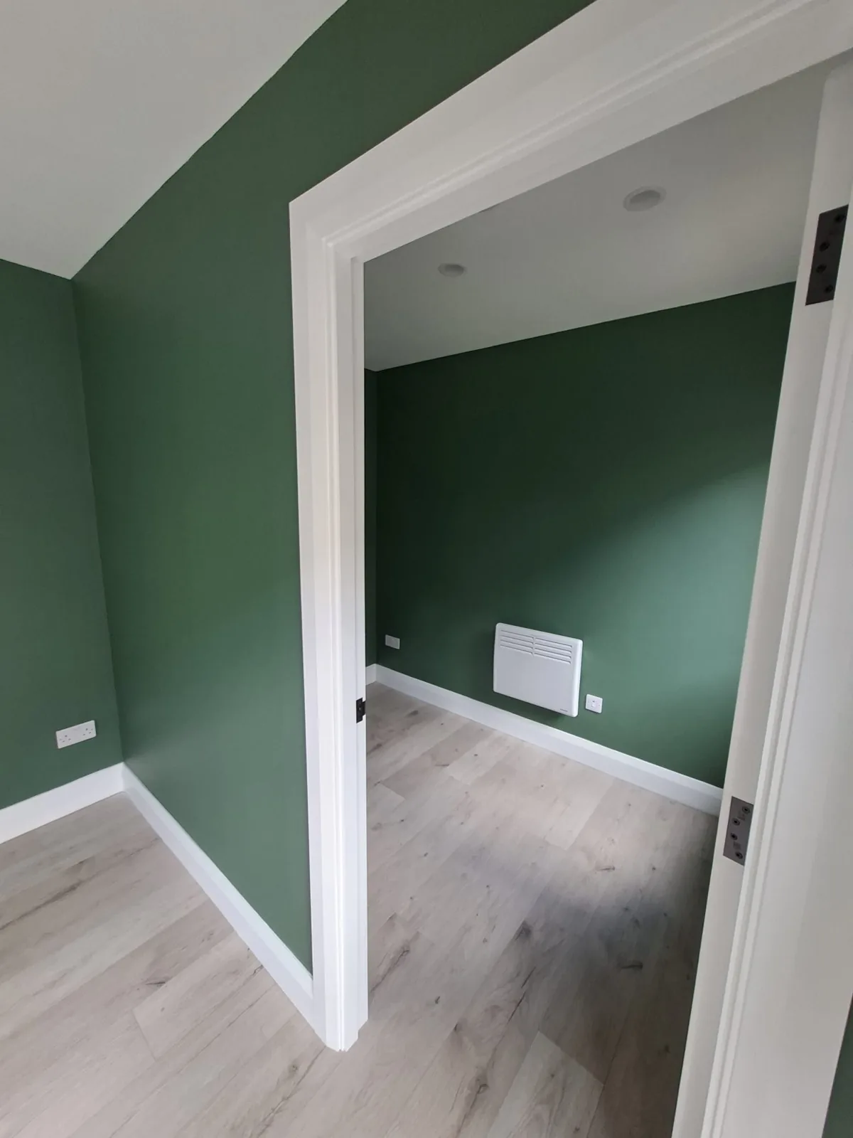 View between finished green-walled rooms with white doorway and pale flooring